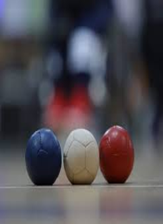 Three Boccia balls—blue, white, and red—placed on an indoor court surface with blurred background, showcasing sports equipment used for precision and Paralympic Boccia training.